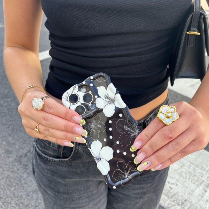 Woman holding Coconut Lane Wavy Phone Case in Mono Flora pattern, wearing floral rings, black top, and jeans.