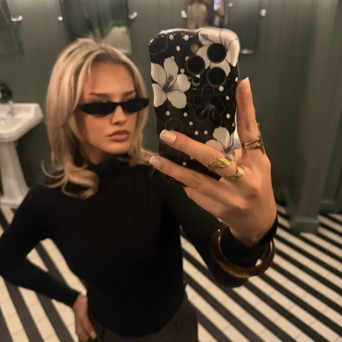 Woman in sunglasses holds a Coconut Lane wavy phone case with a monochrome floral pattern in a mirror selfie.