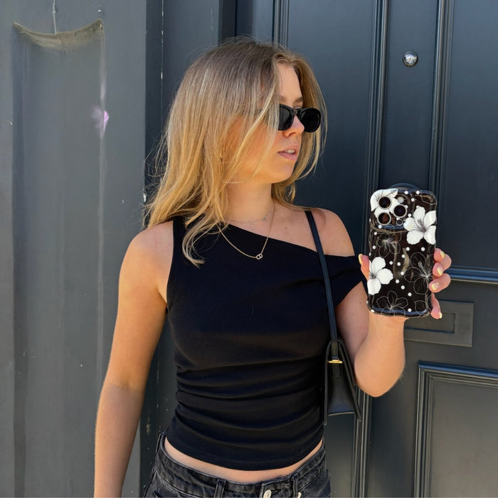 Blonde woman with sunglasses holds a phone in a wavy, monochrome floral Coconut Lane case near a dark door.