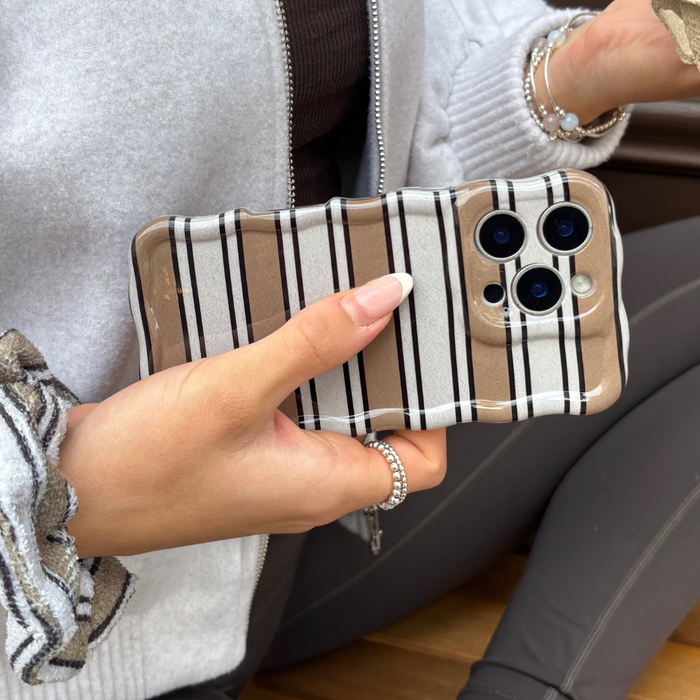 Hand holding phone in Coconut Lane Wavy Phone Case with retro stripes, wearing rings and a bracelet.