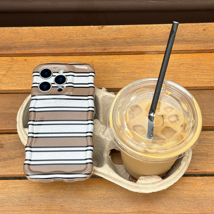 Retro stripe wavy phone case with colorful lines next to iced coffee in a clear cup on a wooden surface.