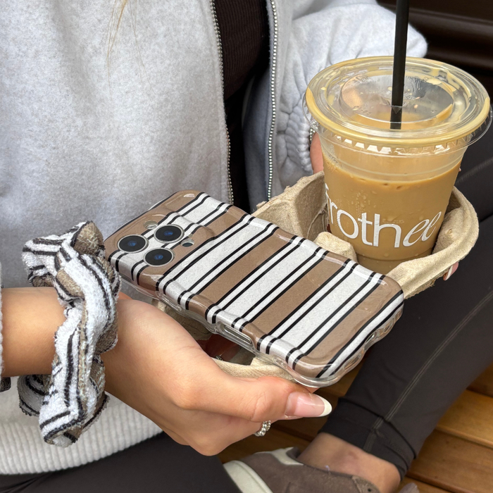 Woman holding an iced coffee and phone with Coconut Lane wavy retro striped case; wearing a gray scrunchie.