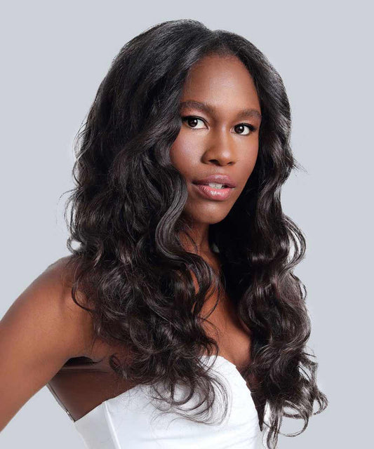 A woman with long, wavy Natural Black  hair styled with hand-tied weft extensions wears a white sleeveless top, gazing forward against a light gray background.