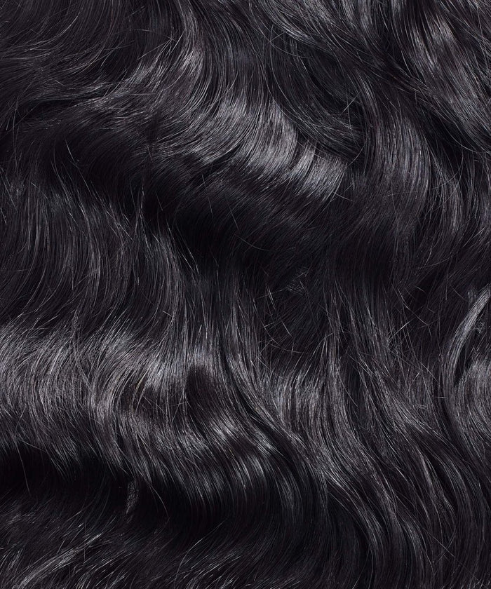 Close-up of Perfect Locks Wavy Virgin Hand-Tied Weft hair extensions with long, black waves, subtle highlights, and a shiny look.